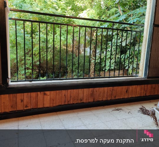 מעקה ברזל שחור עם מסגרת עץ מתחת לחלון פתוח